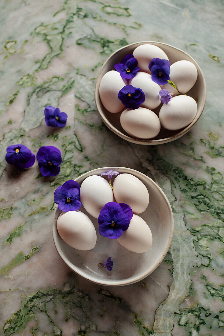 Zwei Schalen mit weißen Eiern dekoriert mit violetten Blüten