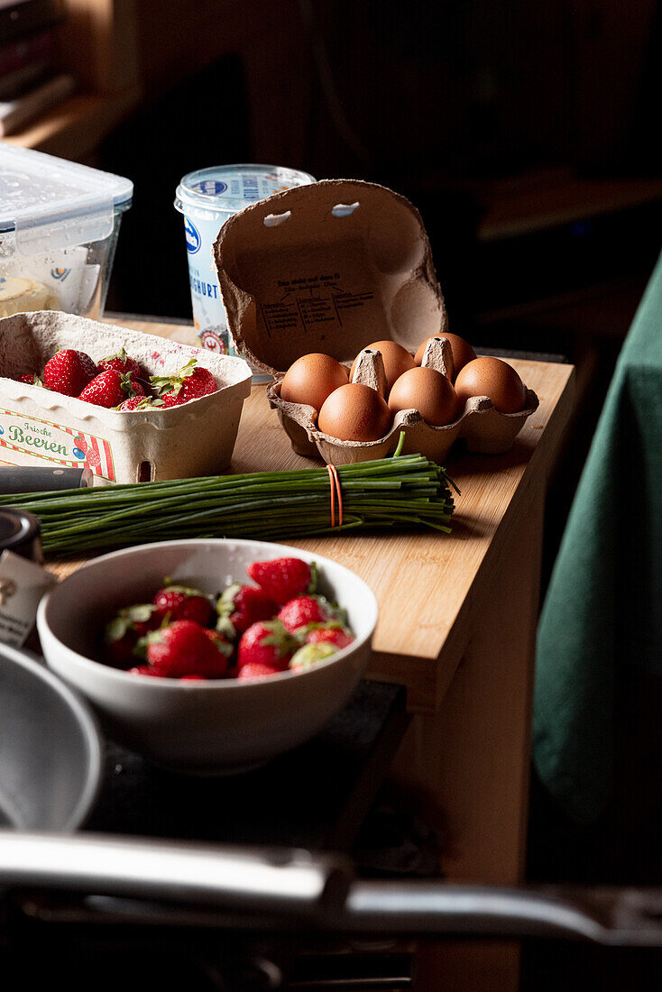 Frische Eier, Erdbeeren und Schnittlauch liegen auf Holztisch