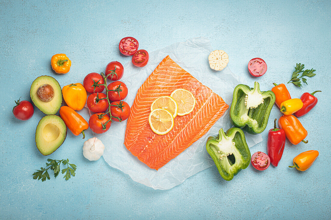 Salmon fillet with lemon slices and fresh vegetables on a light blue background