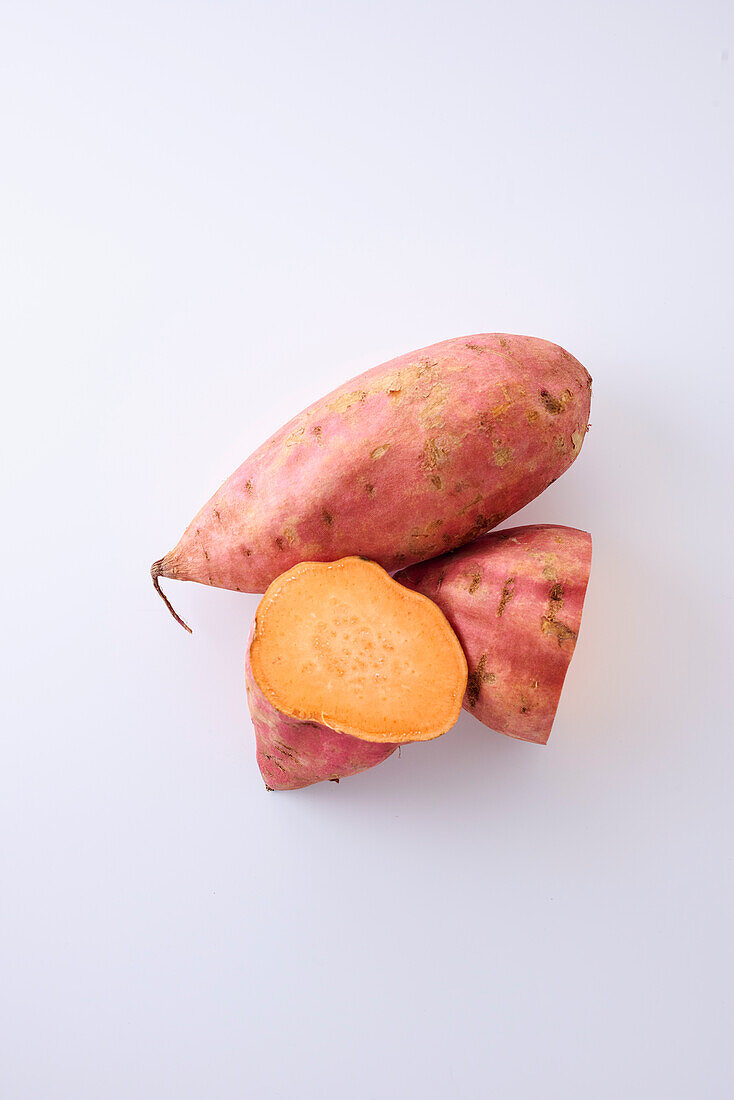 Whole and sliced sweet potatoes on a white background