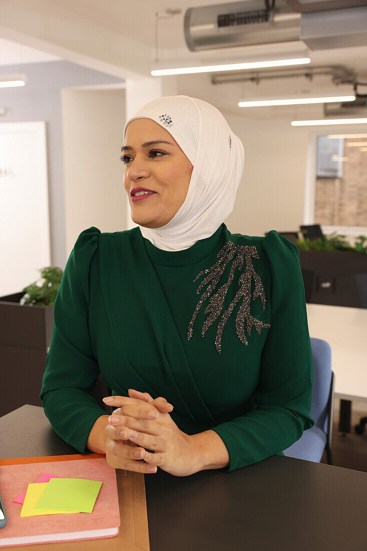 Smiling woman in headscarf sitting at table in modern office