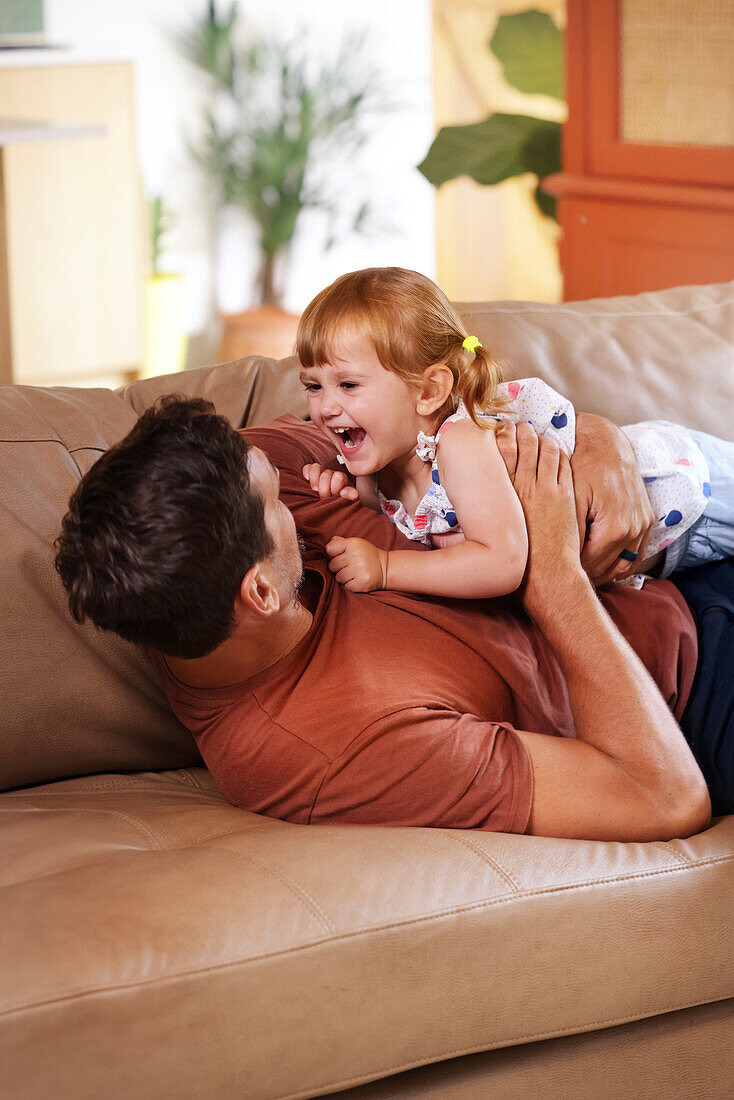 Father playing with daughter on sofa