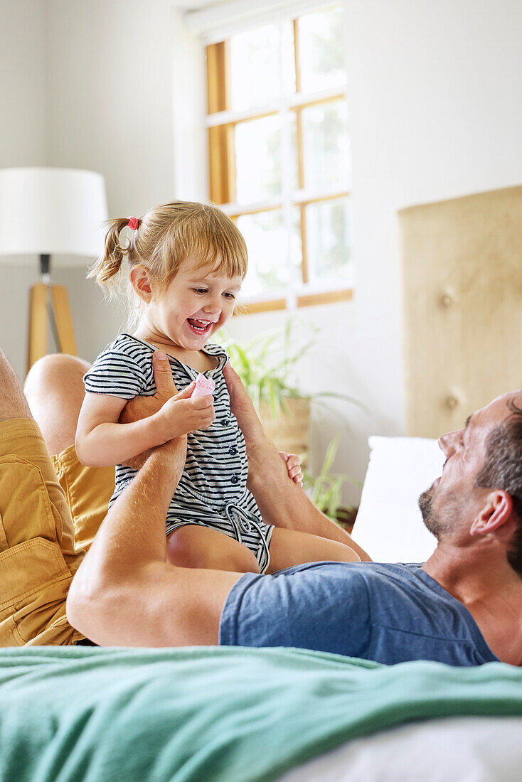 Father playing with daughter on bed