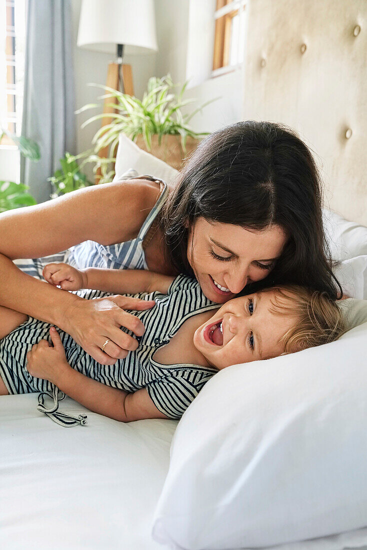 Mother playing with daughter on bed