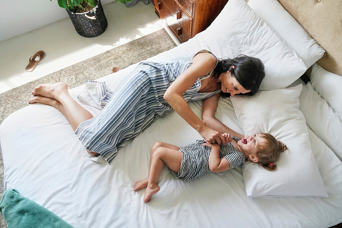 Mother playing with daughter on bed