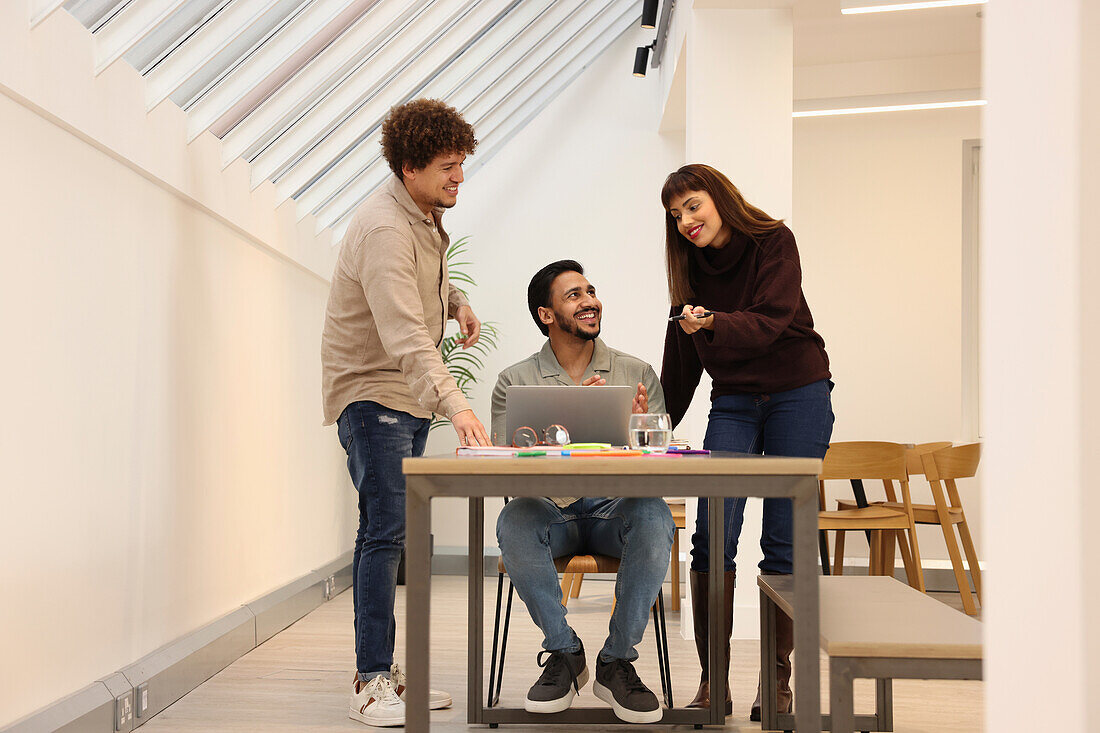 Coworkers looking at laptop at table in office