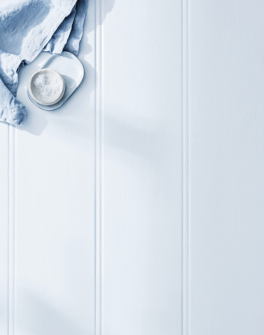 Coarse sea salt and blue tea towel on a white wooden background