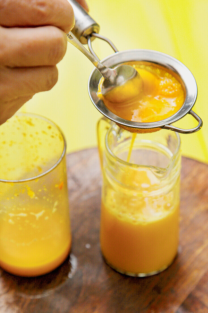 Orange-turmeric juice is poured through a sieve