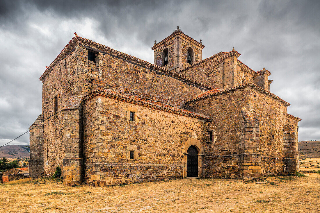 The Gothic church of Nuestra Señora del Rosario stands majestically in Gallinero, Soria, surrounded by rustic countryside and dramatic skies.