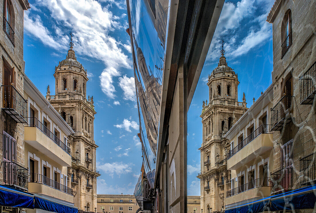 Der Turm der beeindruckenden Kathedrale von Jaen spiegelt sich in einem Schaufenster und zeigt die architektonische Schönheit Andalusiens, Spanien, unter einem strahlend blauen Himmel