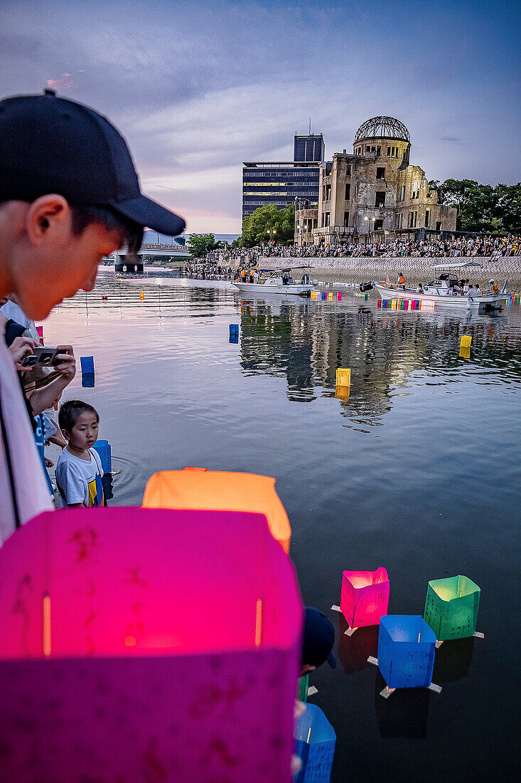 Children float a candle-lit lantern on a river, in front of Atomic Bomb Dome with floating lamps on Motoyasu-gawa River during Peace Memorial Ceremony every August 6 in Hiroshima, Japan