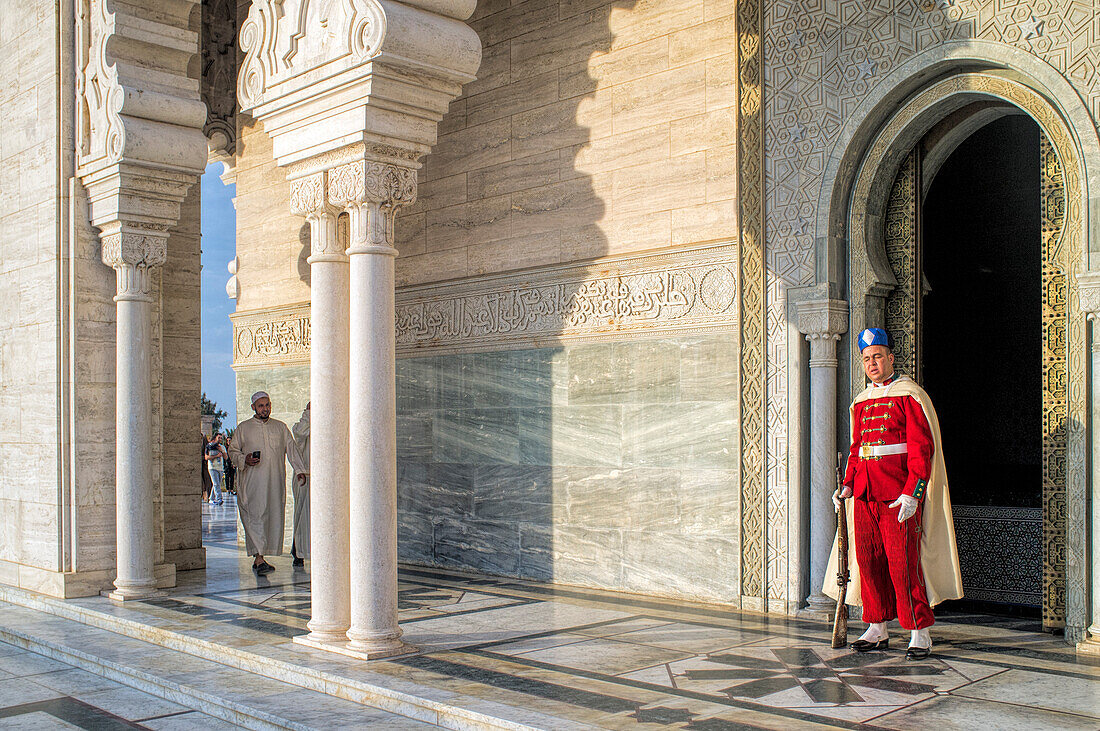 Rabat, Morocco, Apr 24 2015, A guard stands watch at the Mausoleum of Mohammed V, with a visitor walking past on the polished marble floor, as the sun sets.