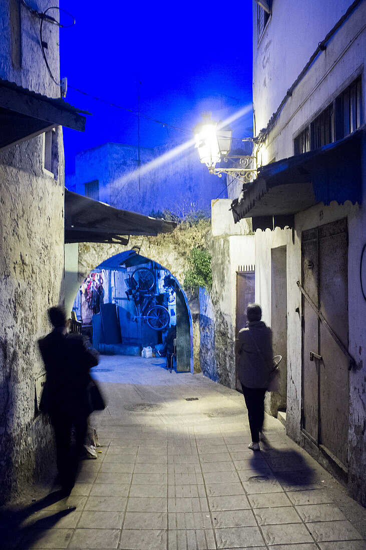 Visitors explore the narrow pathways of Rabat\'s Medina as twilight casts a blue hue over the historic town.