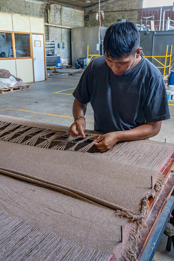 Ein Arbeiter verknotet das Garn von Hand zu Quasten in der Hilandería Warmi, einer Weberei in Palpalá, Argentinien