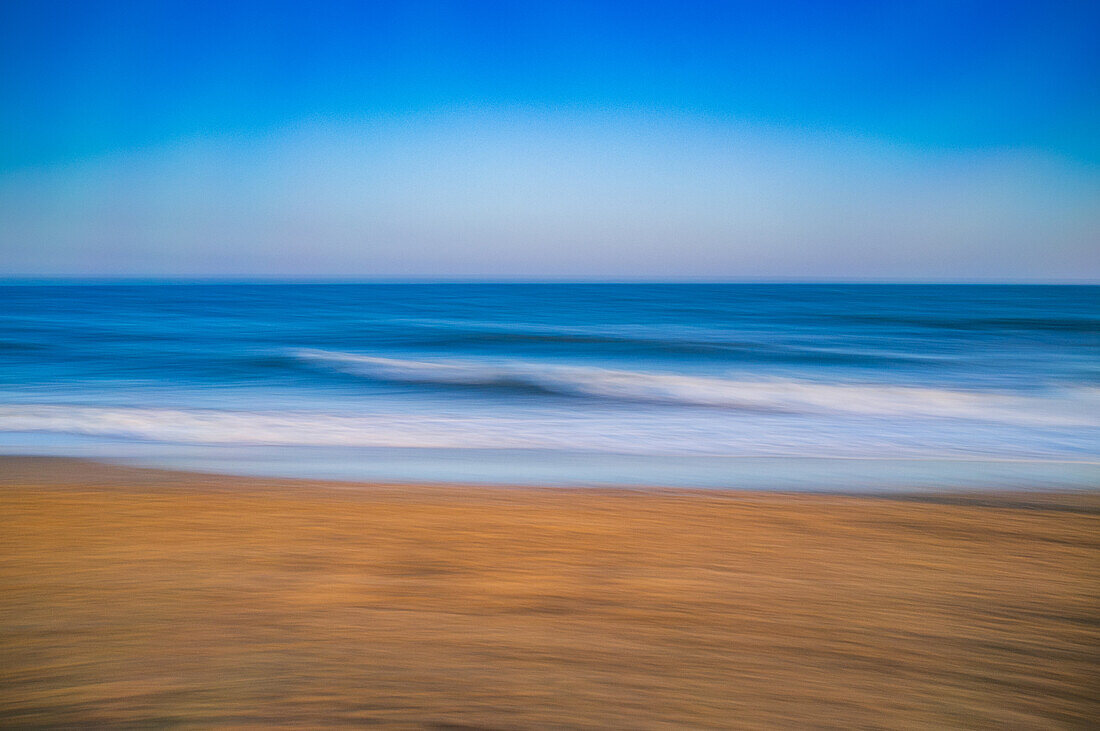 A calming long exposure photograph capturing the gentle waves of the ocean during a beautiful sunset on a sandy beach.