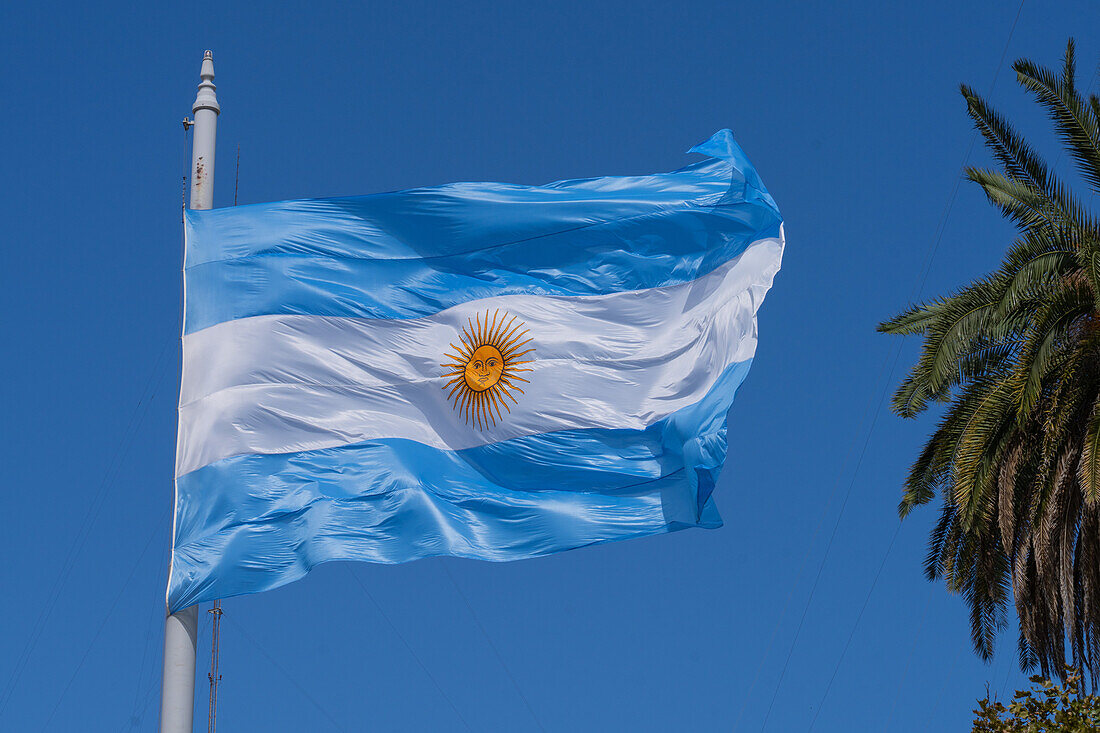 A large Argentine flag flies over the Plaza de Mayo on a sunny day in Buenos Aires, Argentina.