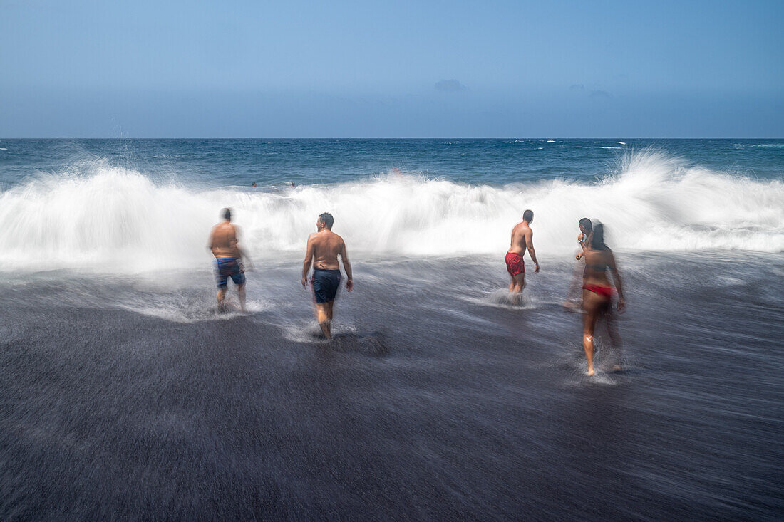 A group of bathers enjoying the waves at Bollullo Beach on the northern coast of Tenerife, La Orotava, Canary Islands, Spain. Long exposure.