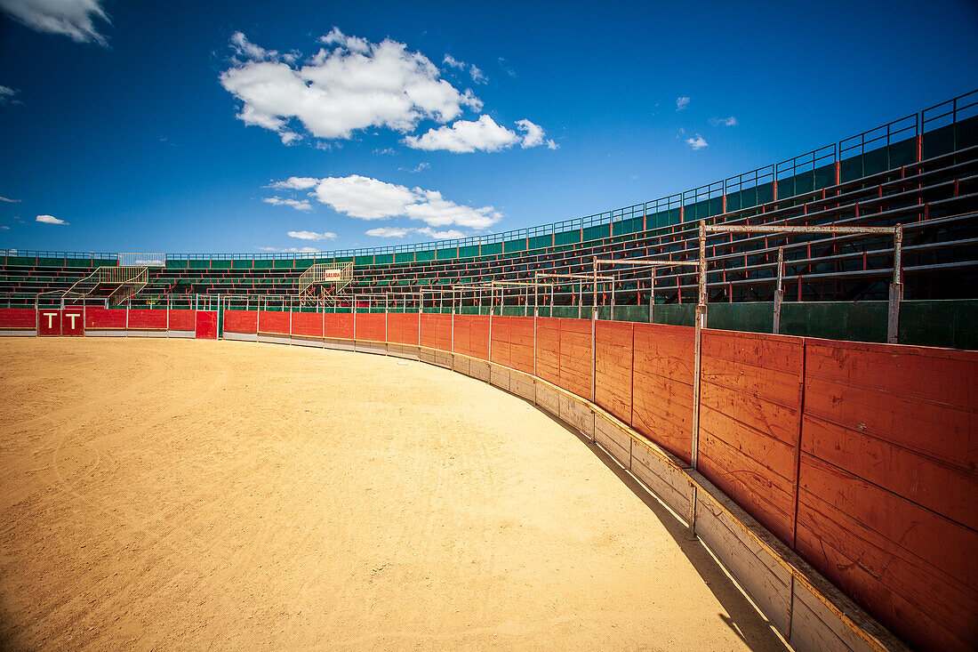 A panoramic view of an empty portable bullring in Aznalcazar, Sevilla, Spain, showcasing the traditional arena under a vivid blue sky.