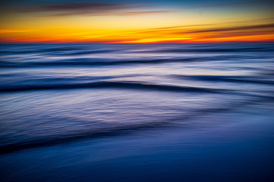 Langzeitbelichtung, die die ruhigen Wellen des Ozeans bei Sonnenuntergang einfängt, mit lebhaften Farben, die sich auf dem Wasser spiegeln und eine friedliche und beruhigende Atmosphäre schaffen