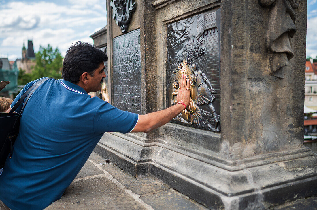 Touristen berühren eine Plakette, die Teil der Statue des Heiligen Johannes von Nepomuk ist, um Glück zu bringen, Prag