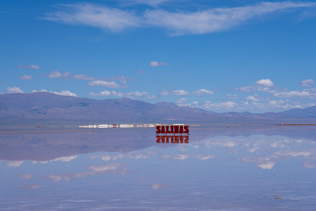 Ein Metallschild auf den Salinen von Salinas Grandes auf dem Altiplano in Argentinien. Die jüngsten Regenfälle haben eine flache Wasserschicht auf den Ebenen hinterlassen. Behnd ist ein Salzabbaubetrieb und die Anden