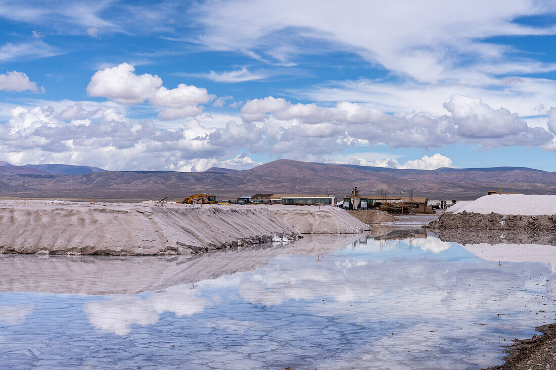 Salt mining operations on the salt flats of Salinas Grandes in northwest Argentina. Clouds are reflected on a shallow sheet of water.