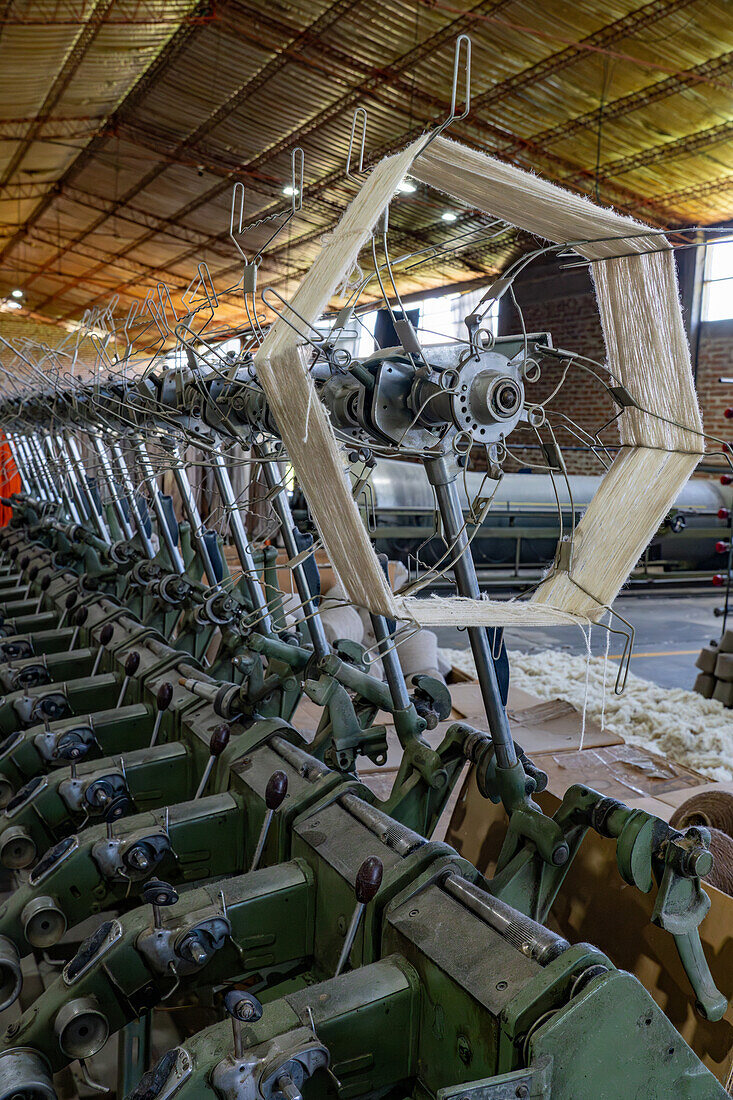 Machinery to spin small bobbins of thread or yarn into larger spools. Hilandería Warmi, a weaving mill in Palpalá, Argentina. The weaving machines use the larger spools.