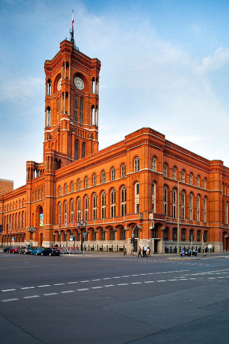 The iconic Rotes Rathaus stands majestically in Berlin, showcasing its striking red façade as people stroll by during the evening.