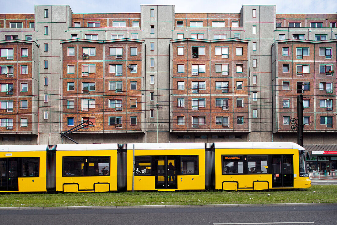 A yellow tram travels along Karl-Liebknecht street, showcasing urban life in Berlin\'s Mitte district beside residential buildings.