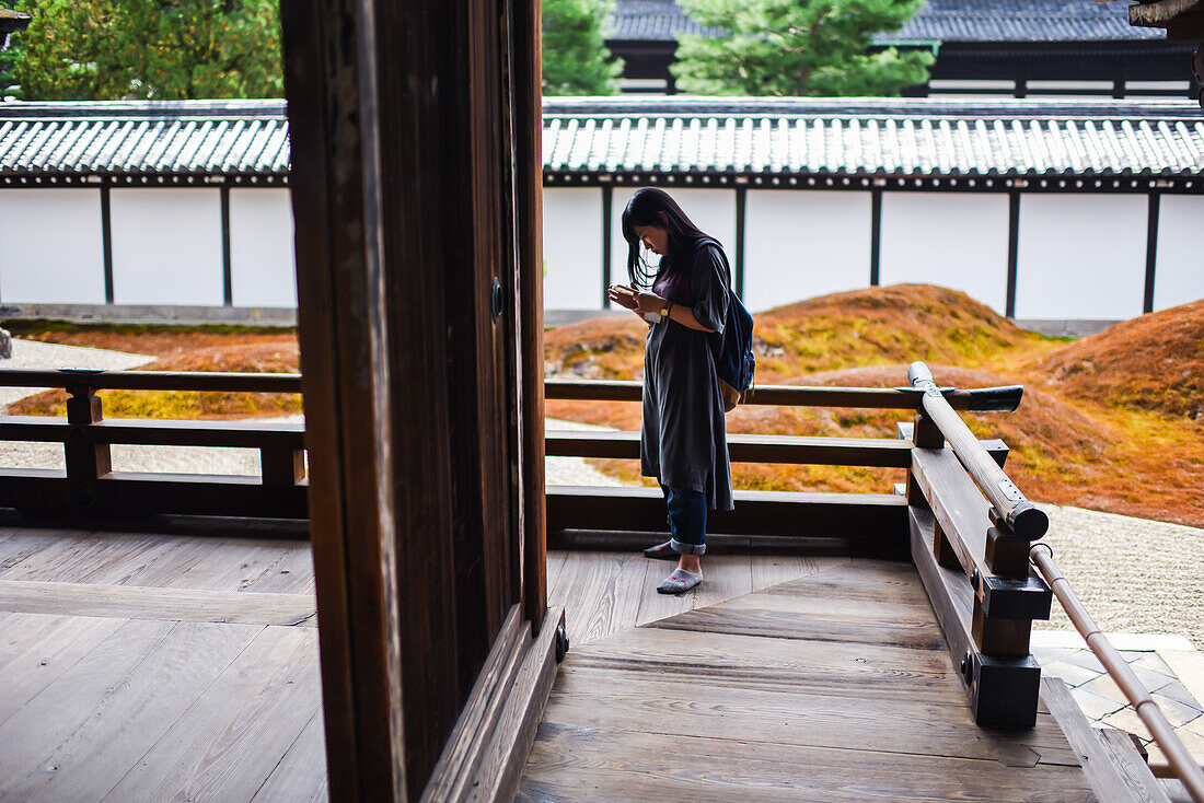 Young woman checking her smartphone at Tofukuji Temple in Kyoto, Japan