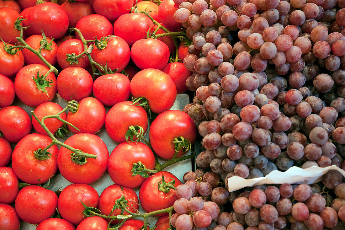 Colorful tomatoes and clusters of grapes displayed at Mercat de la Boqueria, showcasing the vibrant produce of Barcelonas market.