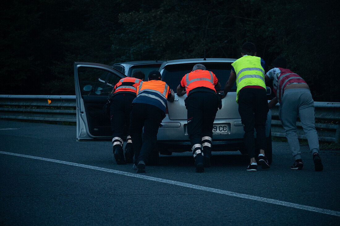 Group of people in safety vest pushing a broken car in road