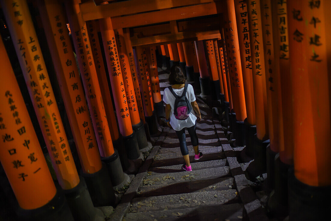 Young caucasian woman exploring Fushimi Inari Taisha temple at night, Kyoto, Japan