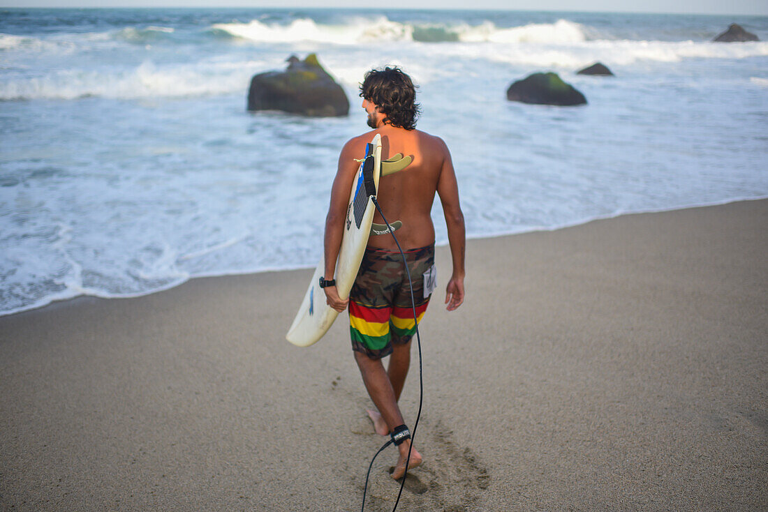 Surfer entering the sea on the beach in front of Finca Barlovento, Tayrona National Park, Colombia