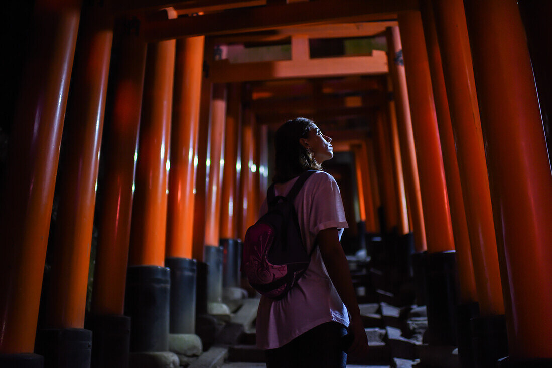 Young caucasian woman exploring Fushimi Inari Taisha temple at night, Kyoto, Japan