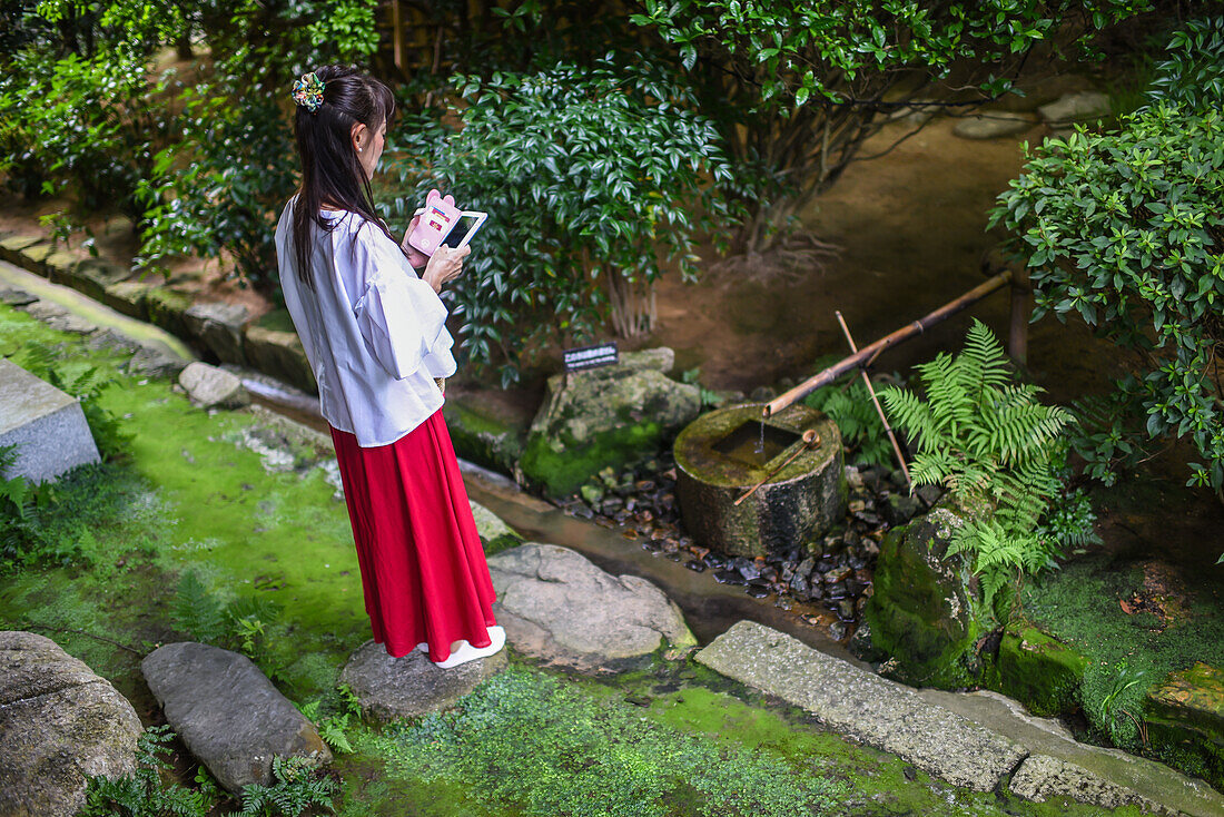 Junge Frau mit Smartphone im Ryoan-Ji-Tempel in Kyoto