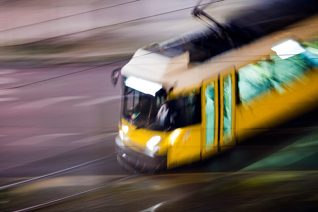 A vibrant tram speeds through the streets of Berlin, creating a ghostly blur against the night sky.