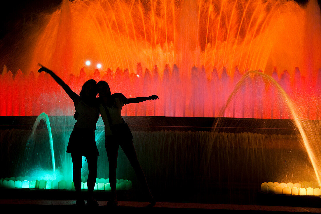 Visitors enjoy the vibrant light show of the Montjuic fountain, surrounded by colorful water jets in Barcelona’s night.