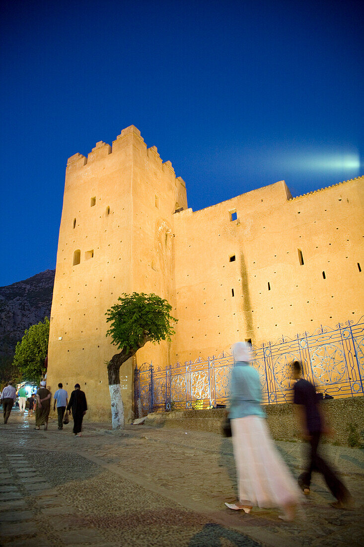 In der Abenddämmerung schlendern Einheimische durch die Kasbah in Chefchaouen und genießen die Abendstimmung und die beeindruckende Architektur