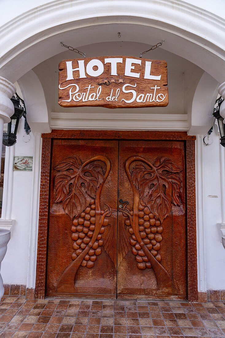 Hand-carved wooden doors with bas relief grape clusters at the entrance of the Portal del Santo Hotel in Cafayate, Argentina.