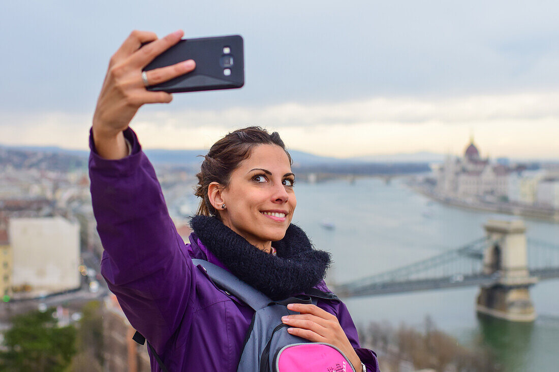 Junge Frau macht ein Selfie mit der Skyline im Hintergrund, einschließlich Parlamentsgebäude und Donau, Budapest, Ungarn, Europa