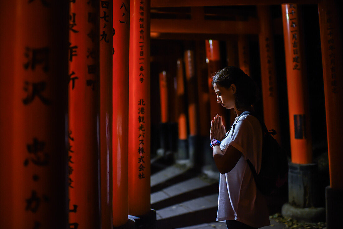 Junge kaukasische Frau, die nachts im Fushimi Inari Taisha-Tempel betet, Kyoto, Japan