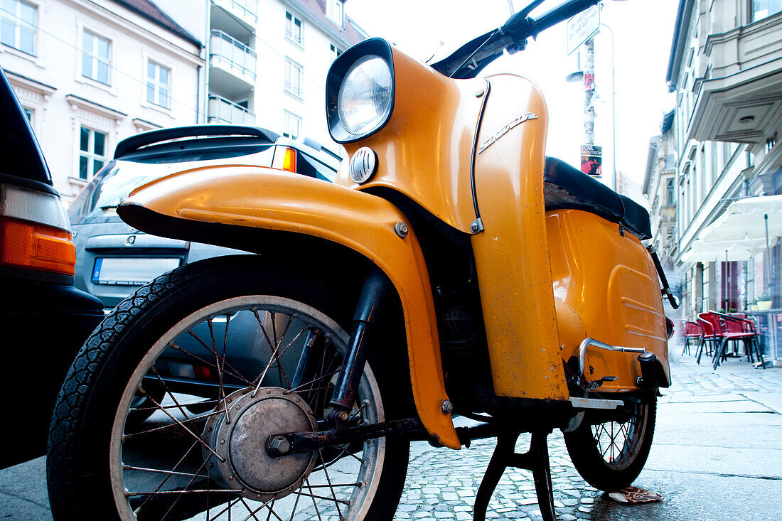 A charming yellow scooter stands parked along the cobblestone streets of East Berlin, evoking nostalgia from a bygone era.