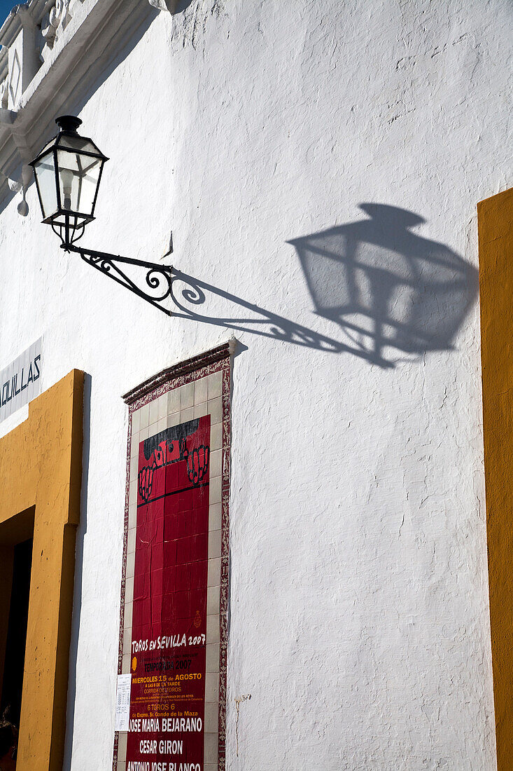 Weiche Schatten von einer dekorativen Laterne beleuchten die weiße Wand der historischen Stierkampfarena Maestranza in Sevilla und verstärken die Atmosphäre