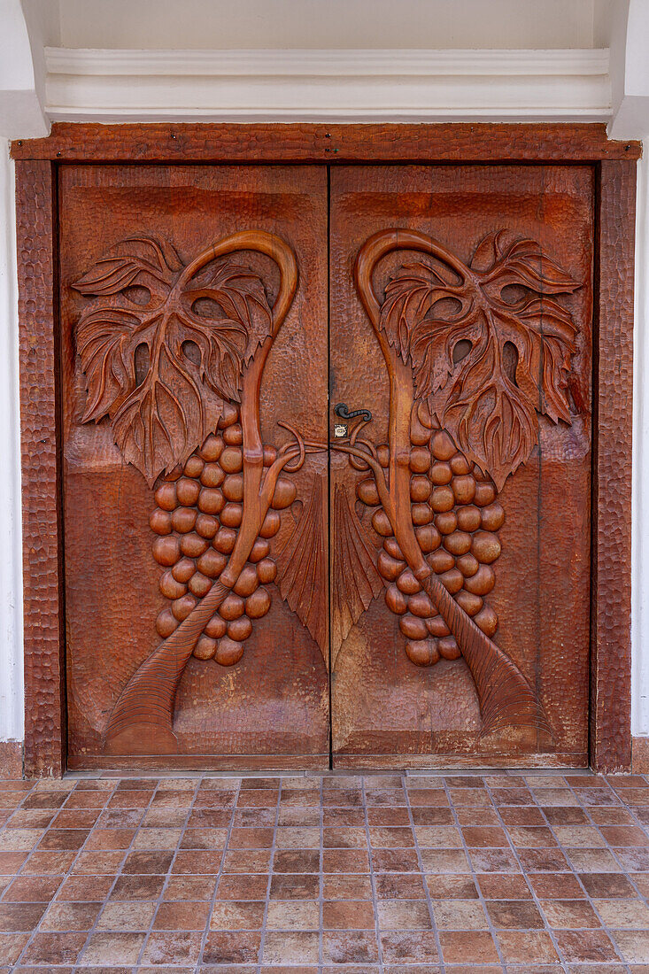 Hand-carved wooden doors with bas relief grape clusters at the entrance of the Portal del Santo Hotel in Cafayate, Argentina.