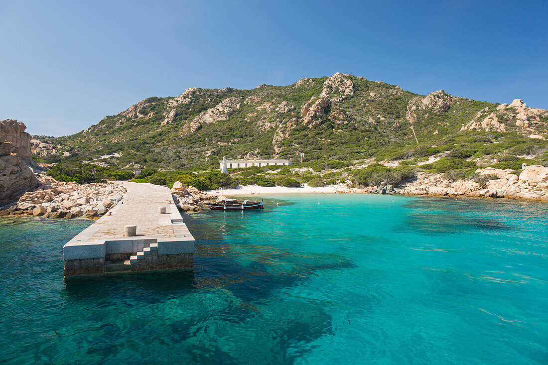 View across clear turquoise water to the fine white sands of the Spiaggia di Punta Rossa Corsara, boat jetty in foreground, Spargi Island, La Maddalena Archipelago National Park, Sassari, Sardinia, Italy, Mediterranean, Europe