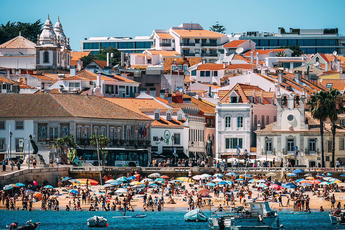 Besucher genießen einen sonnigen Tag am Strand von Cascais, umgeben von bunten Sonnenschirmen und historischen Gebäuden, Portugiesische Riviera, Cascais, 30 km westlich von Lissabon, Portugal, Europa