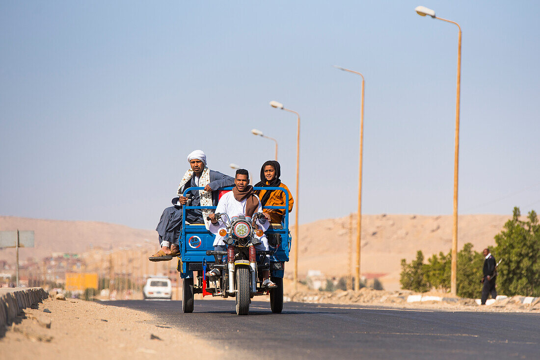 Familie, die auf einem motorisierten Dreirad zu einem Dorf am Nil in der Nähe der Nekropole von El-Kab am Ostufer des Nils fährt, Ägypten, Nordafrika, Afrika