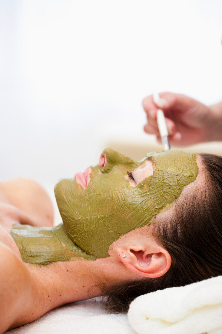 Beautician hand applying green facial mask on woman face