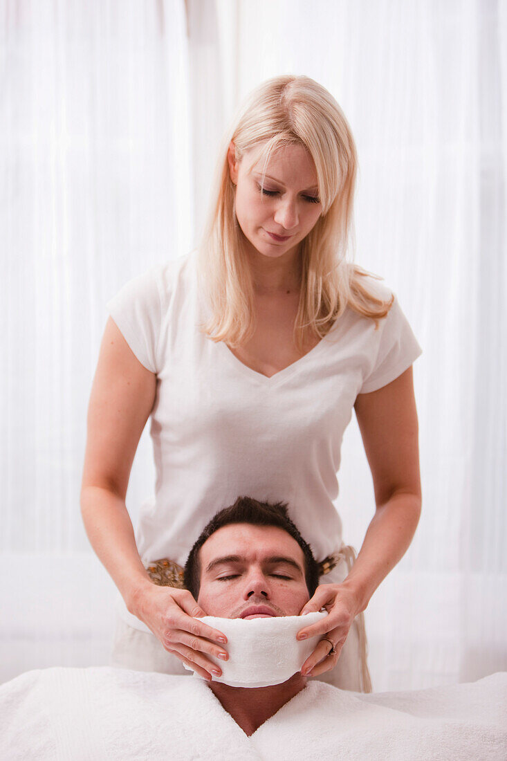 Woman holding hot towel under man chin